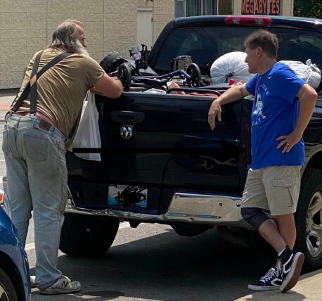 Bill Croyle, right, meets with Robert who leans against his home in July. Skyrocketing prices kept him from renting a house, so he was living in his truck. Croyle runs Walk the Mile, a family charity.