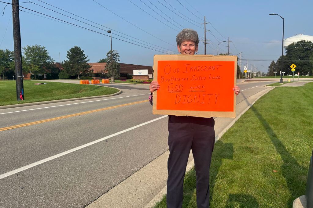 Sister Sally Duffy stands with an orange sign outside an ICE office.
